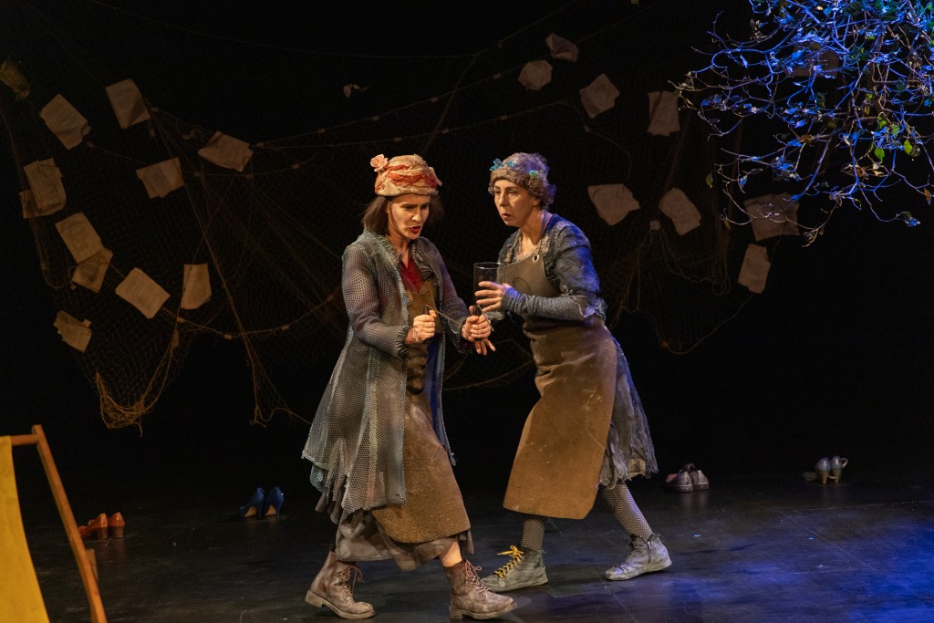 Deux personnes comme en train de marcher ou danser. Derriere elle un filet avec des feuilles et les branches d'un arbre.