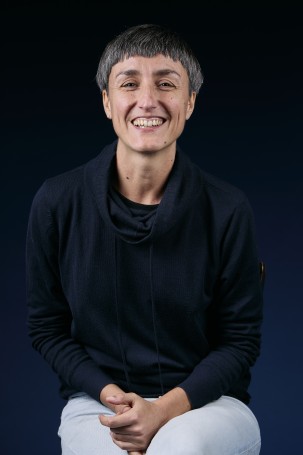 C'est une photo de Àdria Puerto i Molina, responsable billetterie et chargée de production. C'est une femme blanche sur la quarantaine.Elle a les cheveux courts poivre et sel, elle porte un pull noir et un jeans. Elle sourit à plein dents face à la caméra.