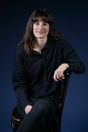 Une photo de Coline Mir, responsable de l'accueil et des buvettes. C'est une femme blanche sur la trentaine.Elle a les cheveux bruns aux epaules et une frange. Elle porte une chemise noire.