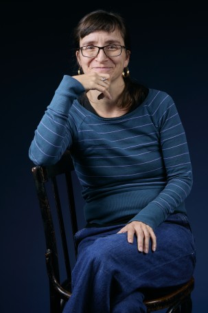 C'est une photo de Laura Sanchez, chargée de communication, responsable presse et redactrice pour le théâtre. Femme blanche sur la cinquantaine. Elle a les cheveux bruns avec une frange, elle porte des lunettes. Elle porte un pull bleu à rayures et un jeans.