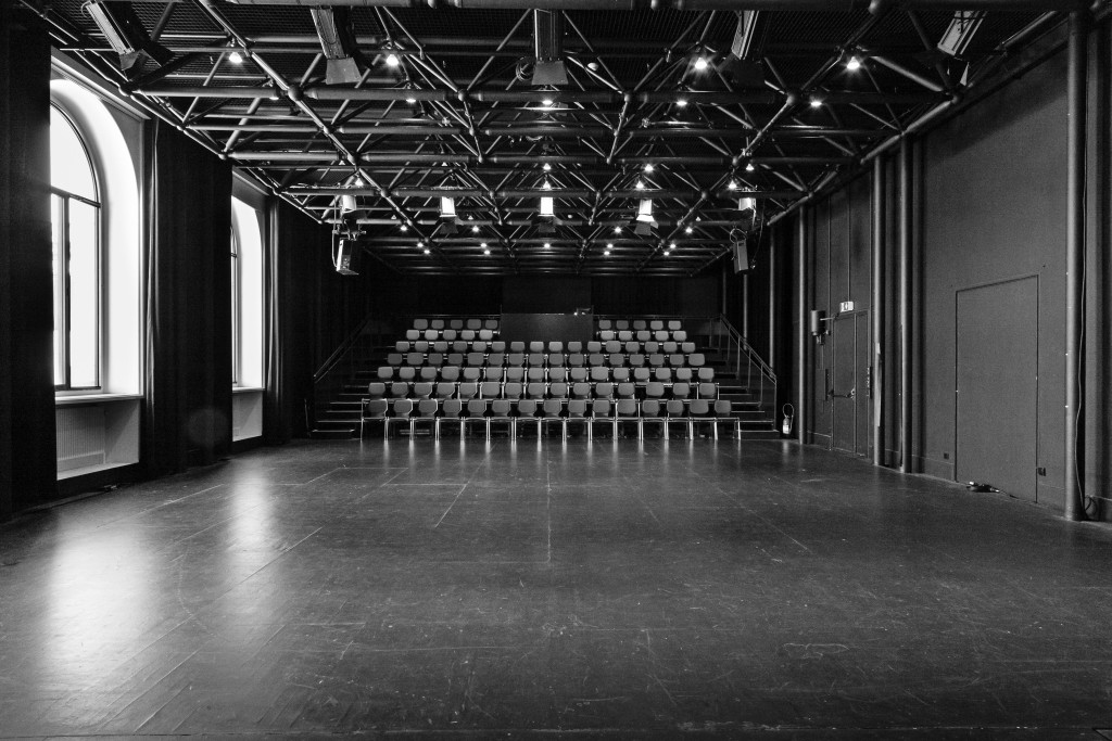 Une photo de la salle du haut depuis le plateau. C'est une boîte noir, les chaises sont noir dans le gradin. le gradin n'est pas très haut.