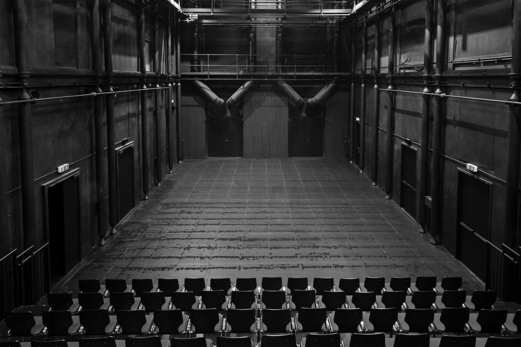 Une photo de la salle du sous-sol prise depuis le public. On voit la scène vide et noire et les premieres rangées de chaises.