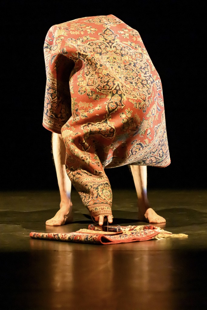 Une personne est en train de s'enrouler dans un tapis. Elle pose sa main par terre comme pour prendre un autre tapis plus petit.