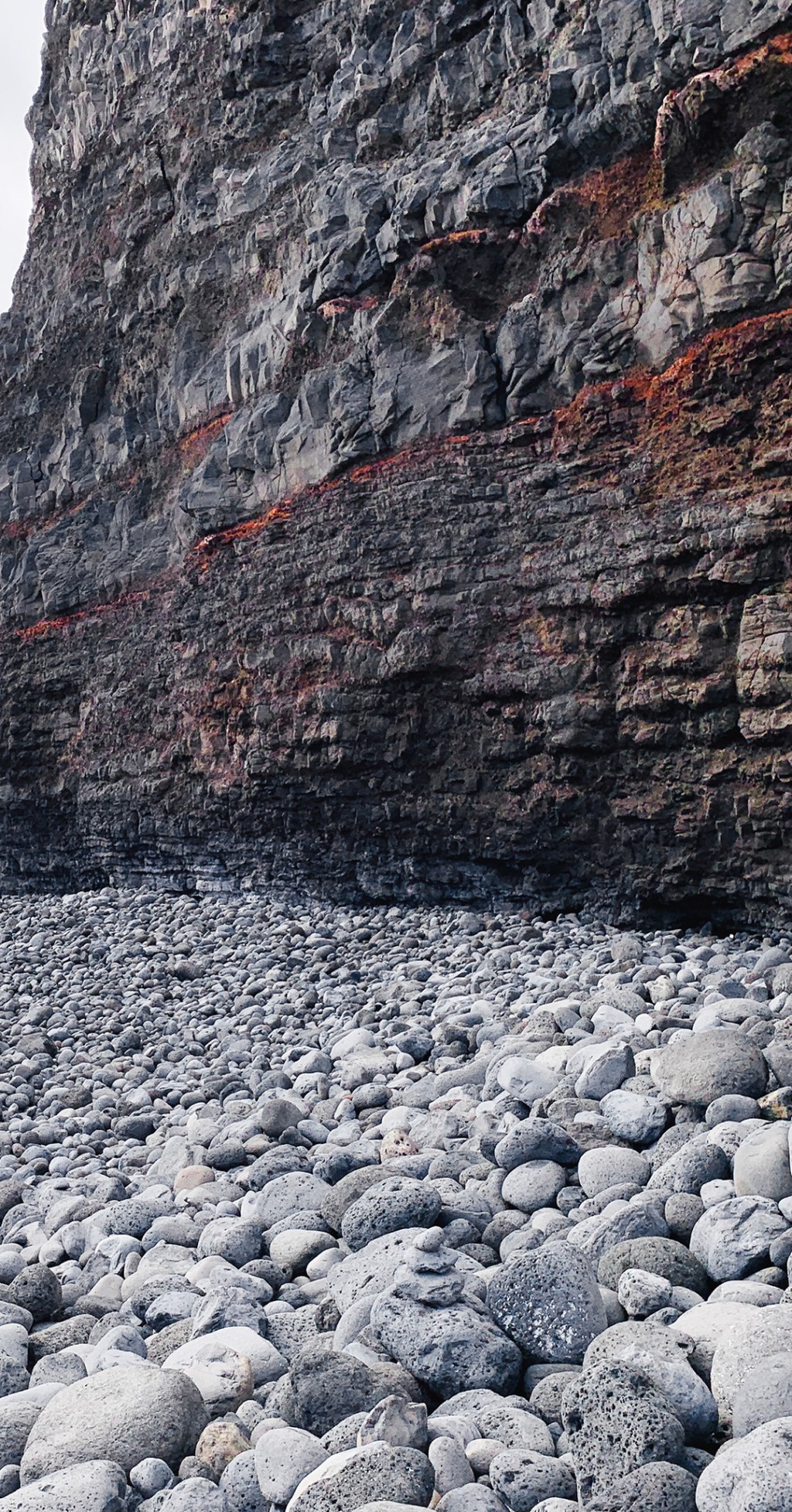 C'est la photo d'une parroi rocheuse et des cailloux. La parroi de roches semble etre contenu par un filet rouge.