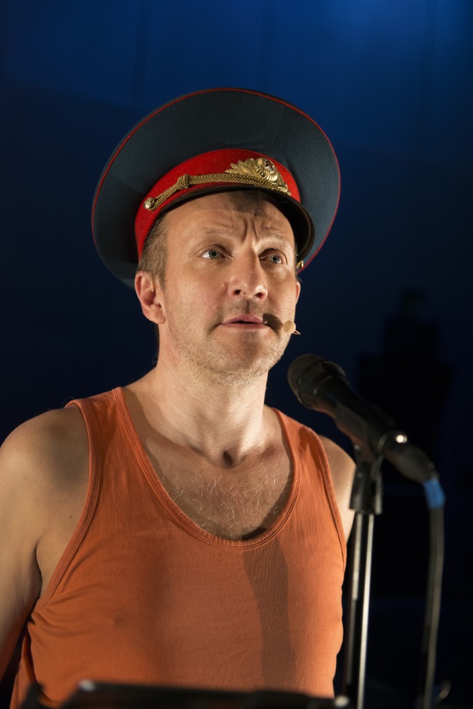 Thierry Romanens en marcel orange avec un chapeau de general militaire en train de parler au micro.