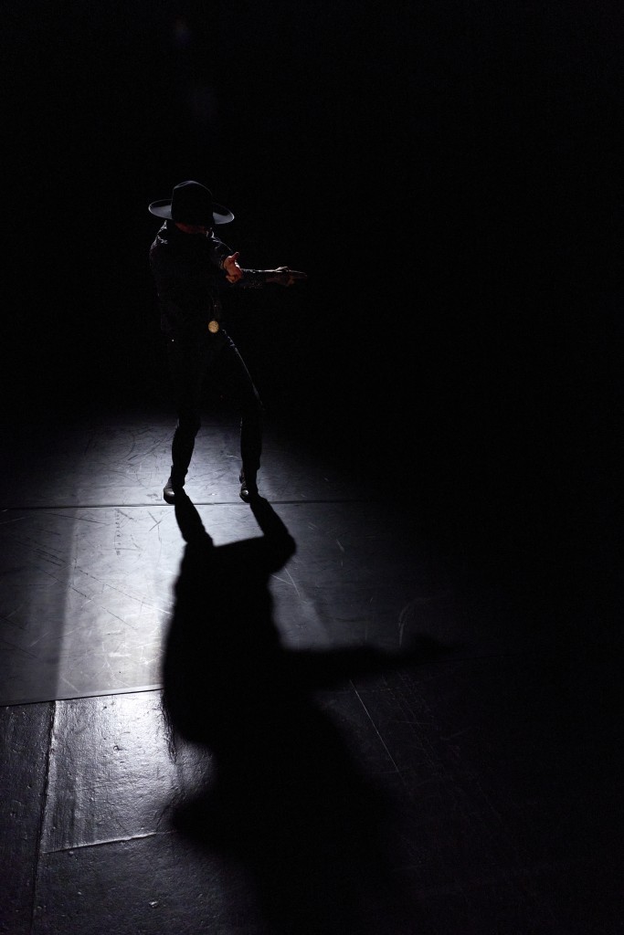 C'est une photo de Nicolas Cantillon en train de danser avec sa guitarre sous le bras. La photo est très sombre.
