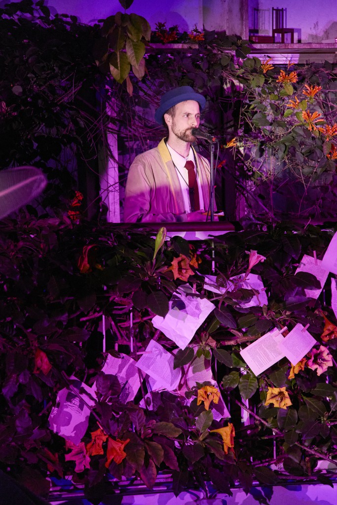 C'est la photo du musicien Thimothée Giddey en train aussi de parler ou chanter au micro. Il est entouré de plantes de fleurs et des feuilles suspendues.