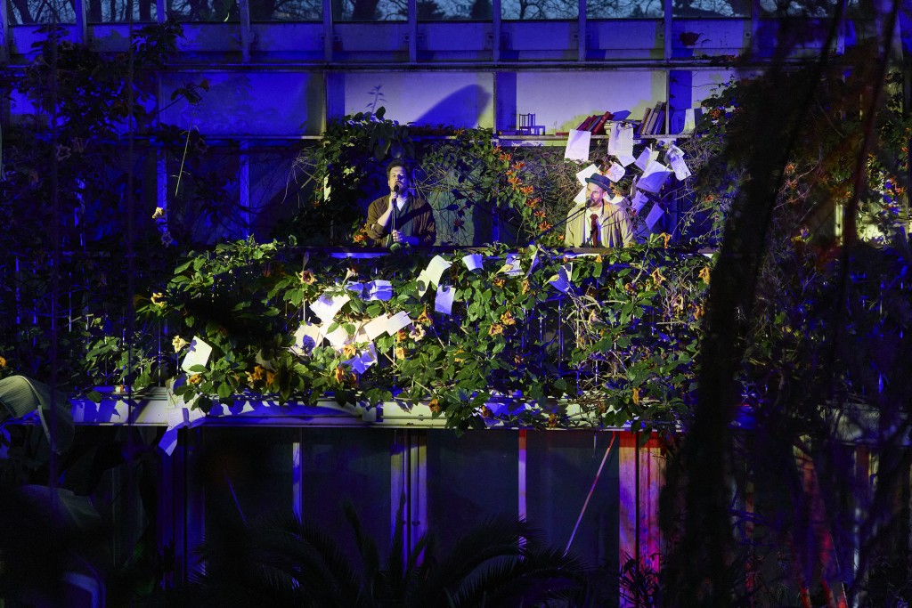 Deux personnes avec des micros, on le voit au loin elles sont éclairées comme sur un balcon et sur le balcon de la vegetation.