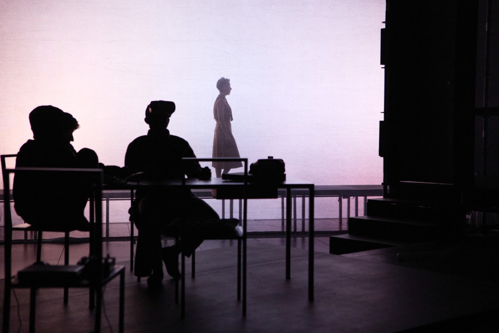 En arriere plan la silhouette d'une personne en train de marcher. Sur le premier plan deux personne assise autour d'une table, mais ce sont des silhouttes noires.