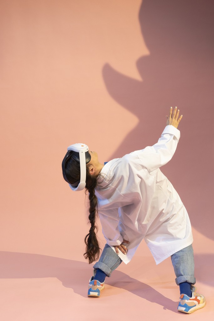 Une personne en blouse blanche avec un casque de ralité virtuelle, elle a une tresse et elle se penche en arrière.