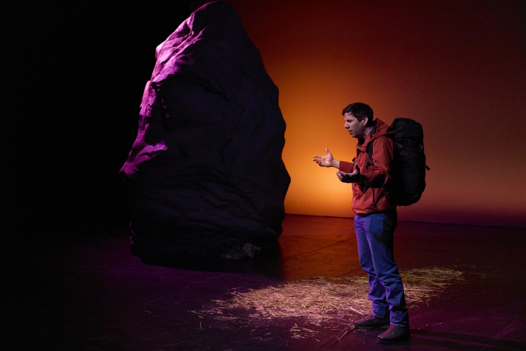 A gauche de la photo un rocher, à droite un homme, comme un promeneur avec un sac à dos et une veste coupe vent.