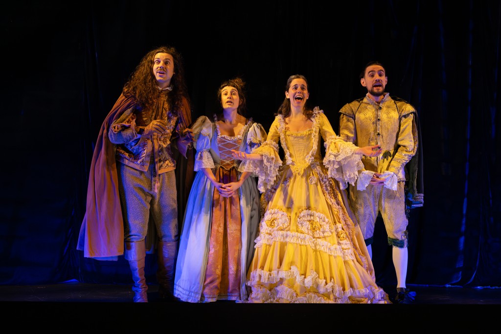 Quatre personnes en costumes d'époque style Louis XiV sont en train de chanter une chansons. Elles sont face au public.