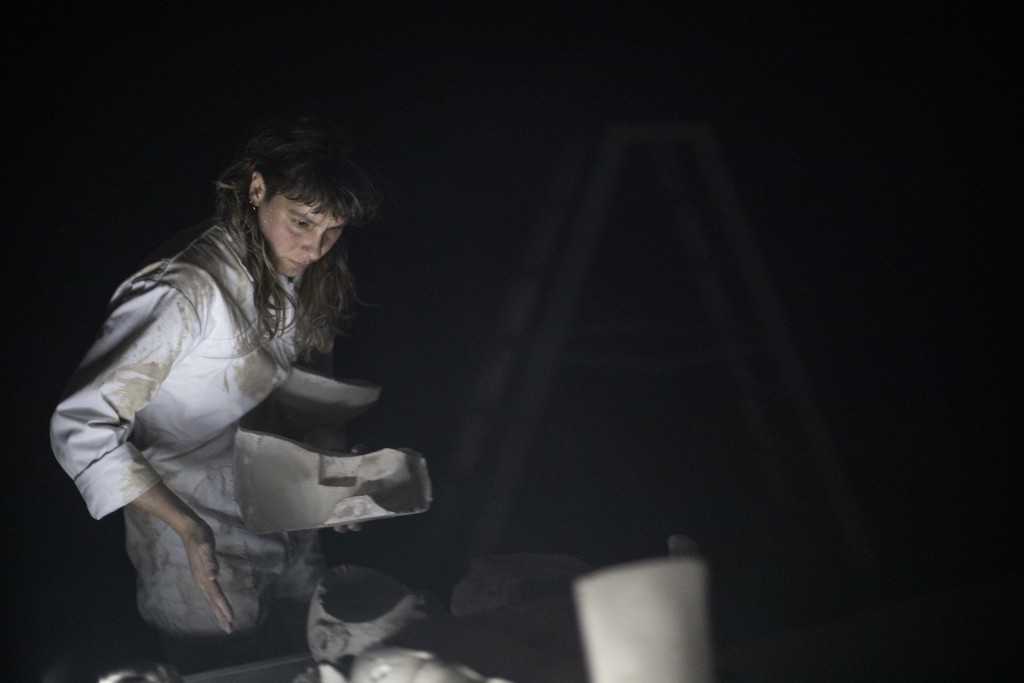 Une personne avec une combinaison blanche est en train de construire quelque chose avec une matiere qui pourrait resembler à l'argille