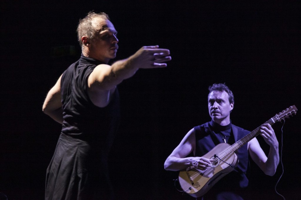 A gauche une personne en train de danser habillée en noir, à droite une personne en train de jouer un instrument à cordes qui ressemble à une guitarre.