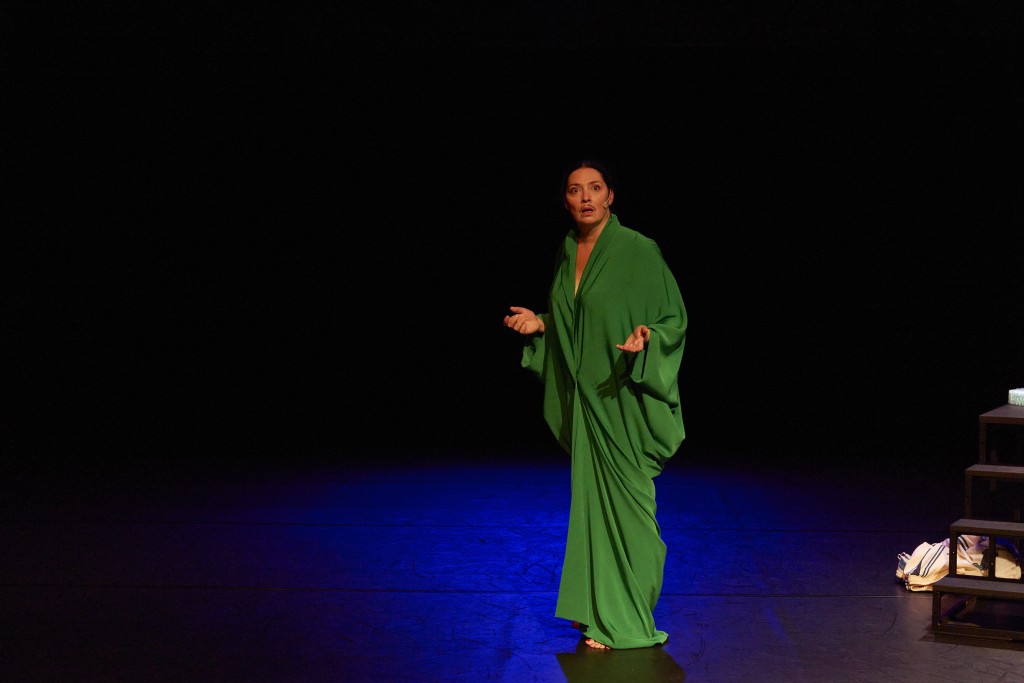 C'est une personne habillée avec une robe longue verte. Elle est en train de parler en ouvrant les bras.
