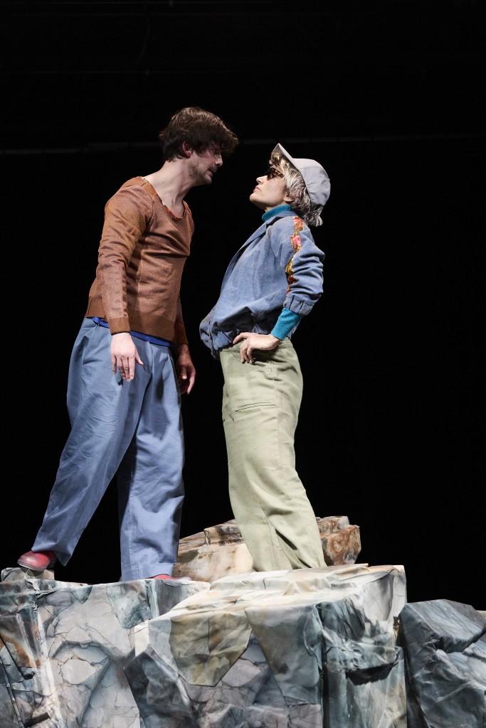 Dans cette image à gauche le comédien Simon La Barriere, à droutre la comedienne Verena Lopes. La comedienne est deguisée, elle porte un chapeau, une perruque blonde et des lunettes de soleil. Simon est comme en train de crier sur elle, mais elle n'a pas l'air appeurée au contraire elle se tient bien droite avec les mains aux hanches.