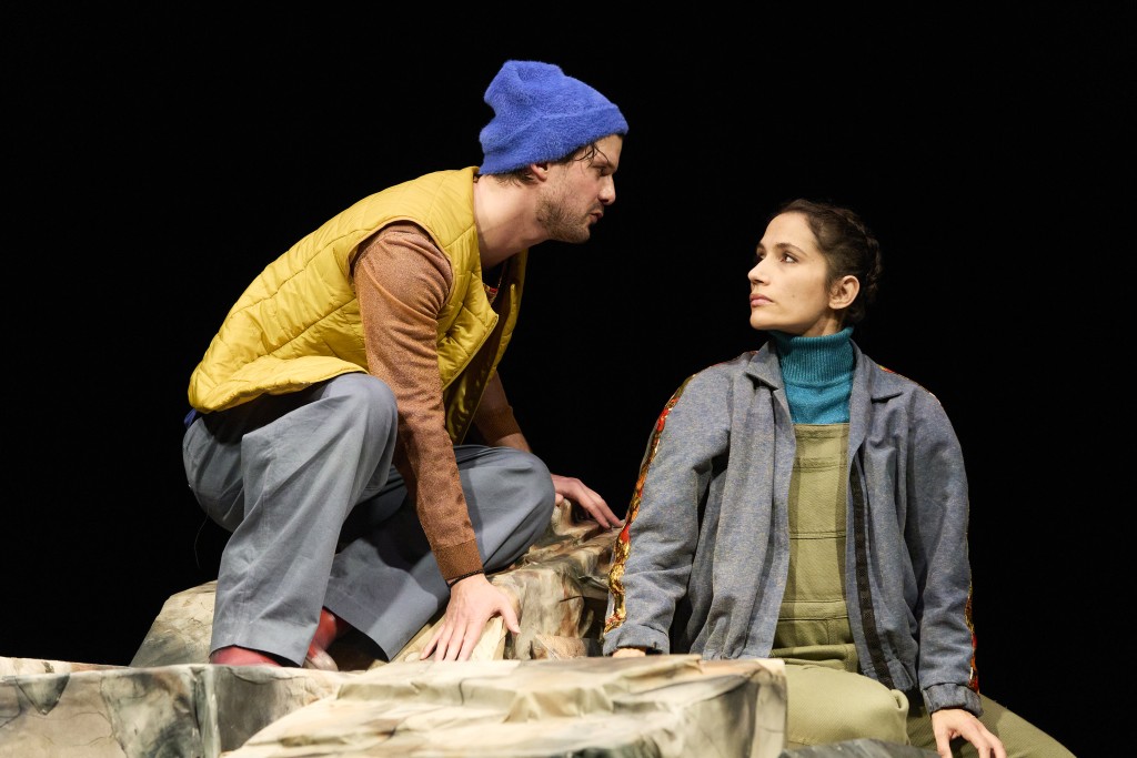 Sur cette image à gauche le comedie Simon La Barriere à droite la comedienne Verena Lopes. Les deux sont assis et se regardent donc on voit leurs profils. Simon porte un bonnet bleu et un gilet jaune, Verena une veste sportive grise. Les artistes ont l'air serieurse.