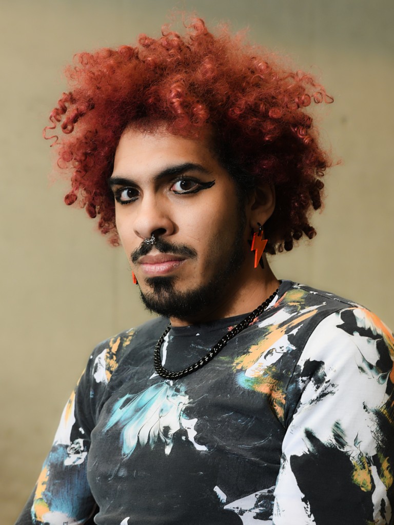 C'est la photo d'une personne qui a la coupe afro rouge. Elle porte des boucles d'oreille. Un t-shirt colorée et un beau maquillage. Cette personne est Edwin Ramirez.