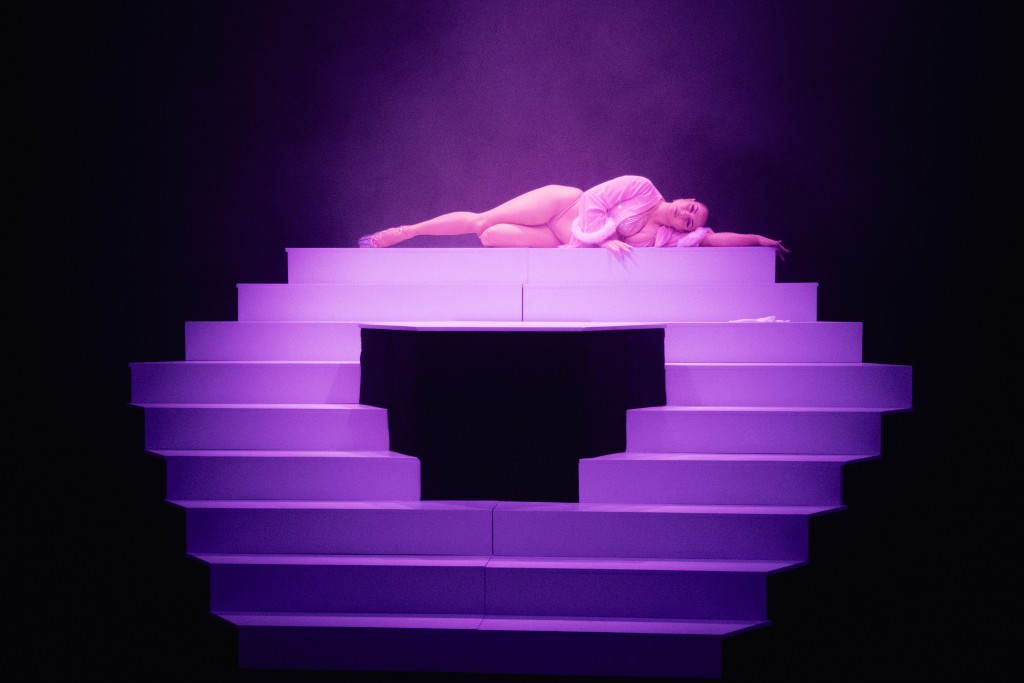 Un escalier immergé dans une lumière violette. Une personne au bout de l'escalier par terre allongée.